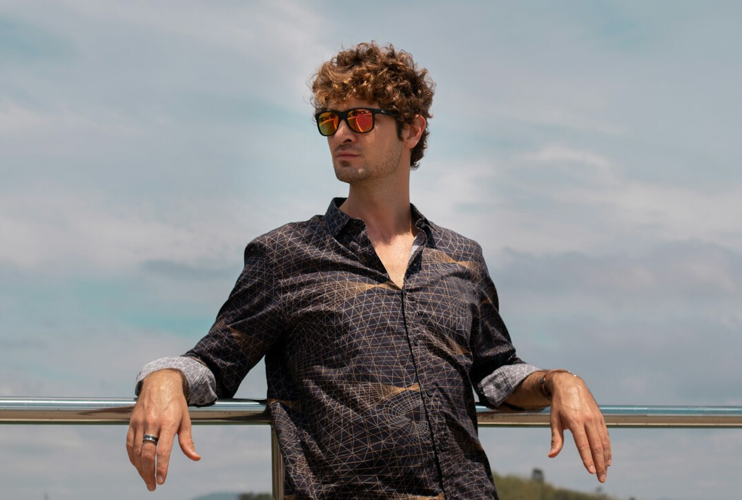 Smiling man with curly hair and glasses in a patterned shirt